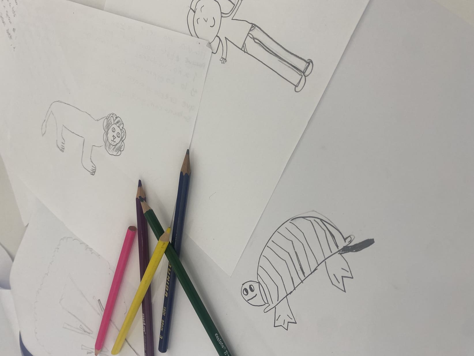 Dibujos a lápiz de un niño —un león, una tortuga y una figura humana— sobre folios en la mesa de la consulta, con cinco lápices de colores cruzados encima