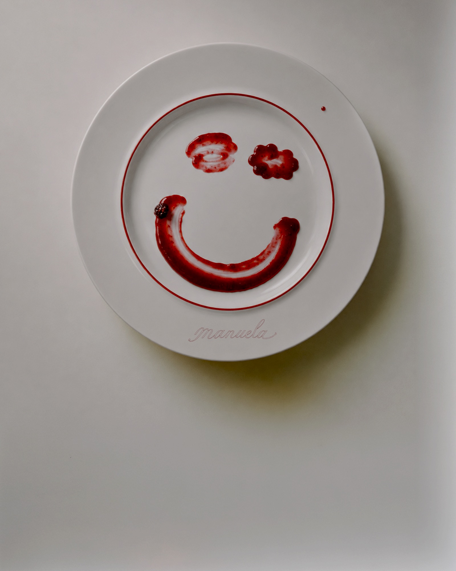 Plato blanco con una cara sonriente pintada con mermelada de frambuesa y el nombre Manuela