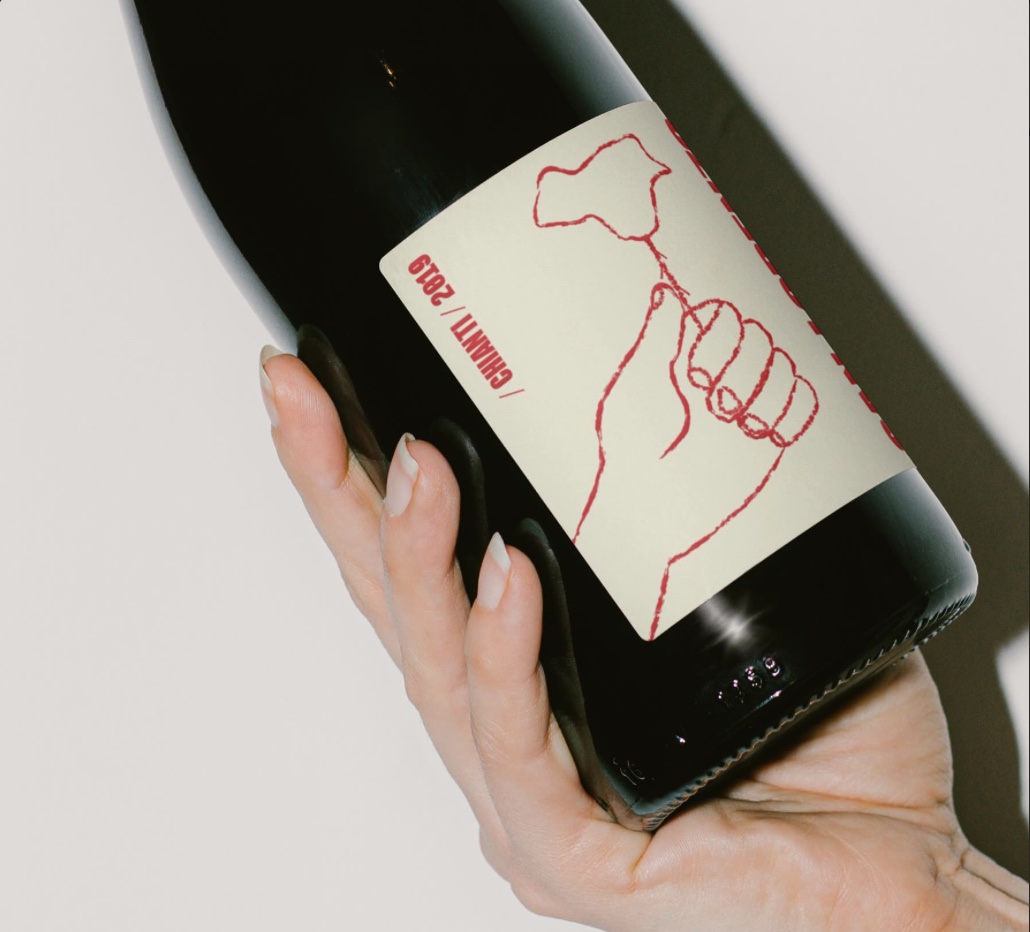 Botella de San Lorenzo en la mano: etiqueta crema con una mano que sostiene una rosa dibujada en rojo